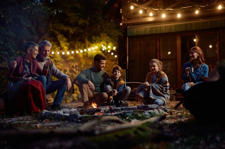 Happy multigeneration family gathering around campfire and roasting corn in the evening