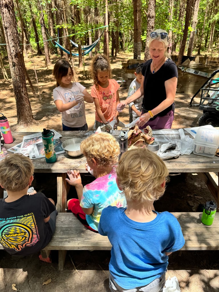 Adult leading outdoor craft activity with children around picnic table in forest campsite setting
