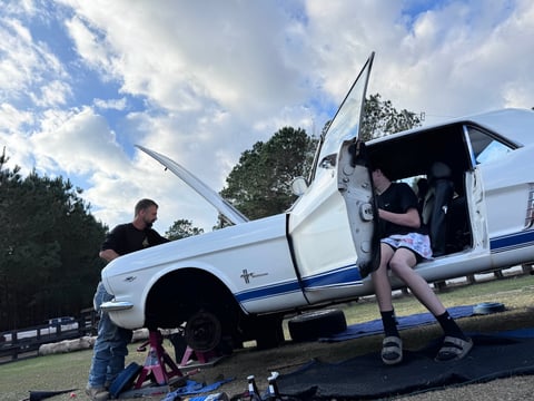 White and blue classic pickup truck with open doors at an outdoor event, with people standing nearby