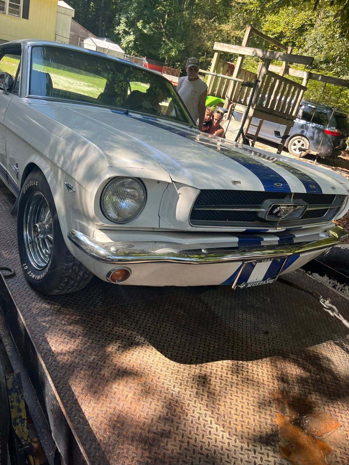 White and blue 1960s Ford Mustang with racing stripes parked in driveway