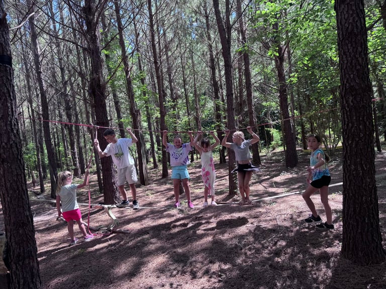 Group of children and adults exercising outdoors in a wooded forest area with tall trees and natural ground cover