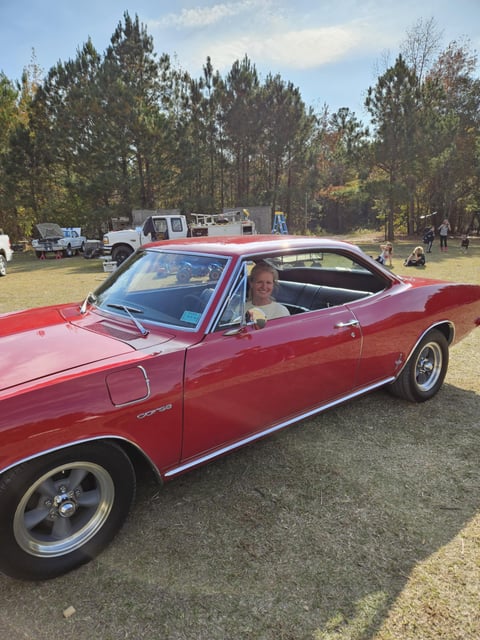 Red vintage convertible car at outdoor car show with pine trees in background